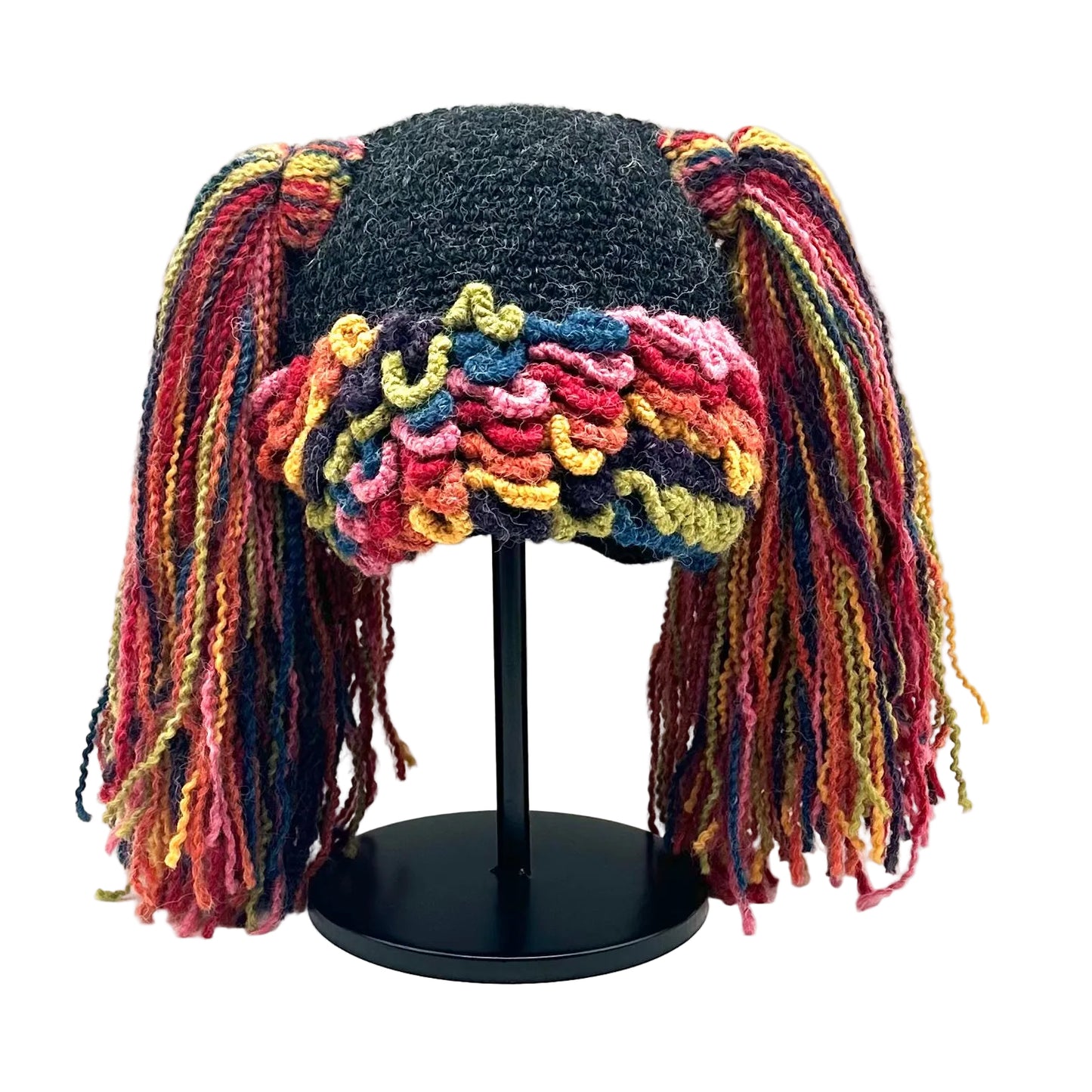 Colorful knitted hat with long strands on a black stand against a white background