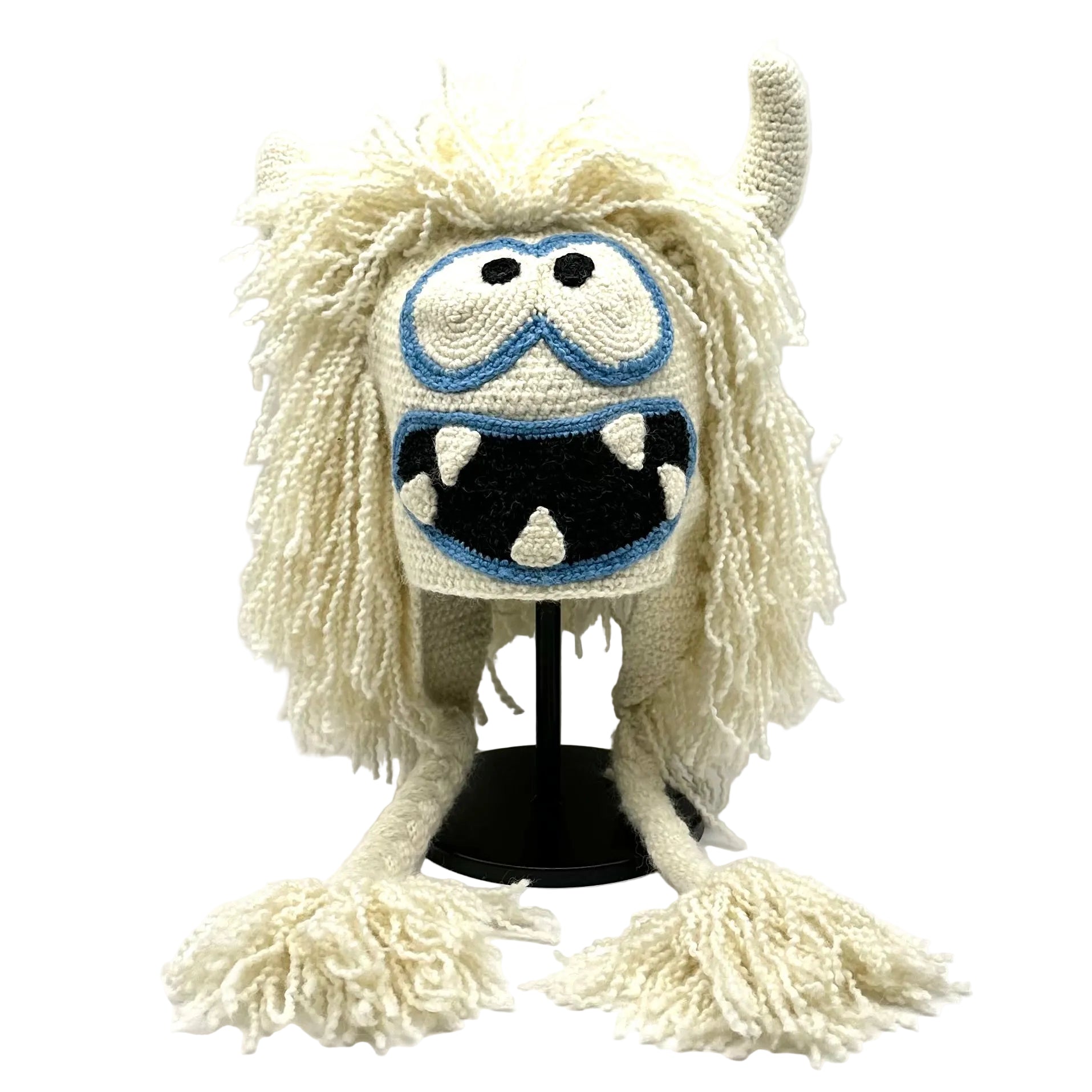 Monster-themed knitted hat with white fur and blue goggles on a white background