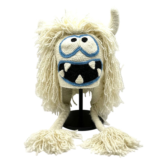 Monster-themed knitted hat with white fur and blue goggles on a white background