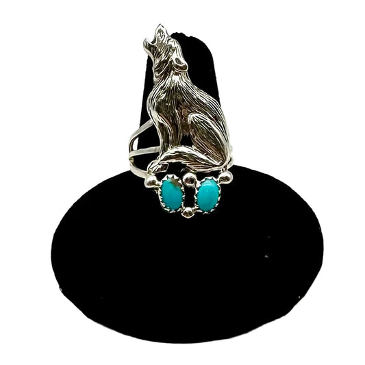 Silver ring with a wolf design and turquoise stones on a black stand against a white background