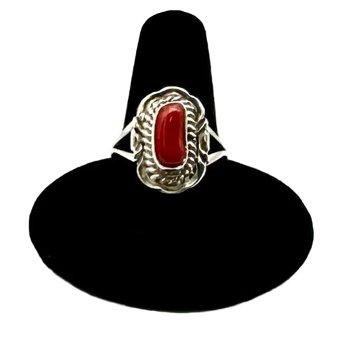 Silver ring with a red stone on a black stand against a white background