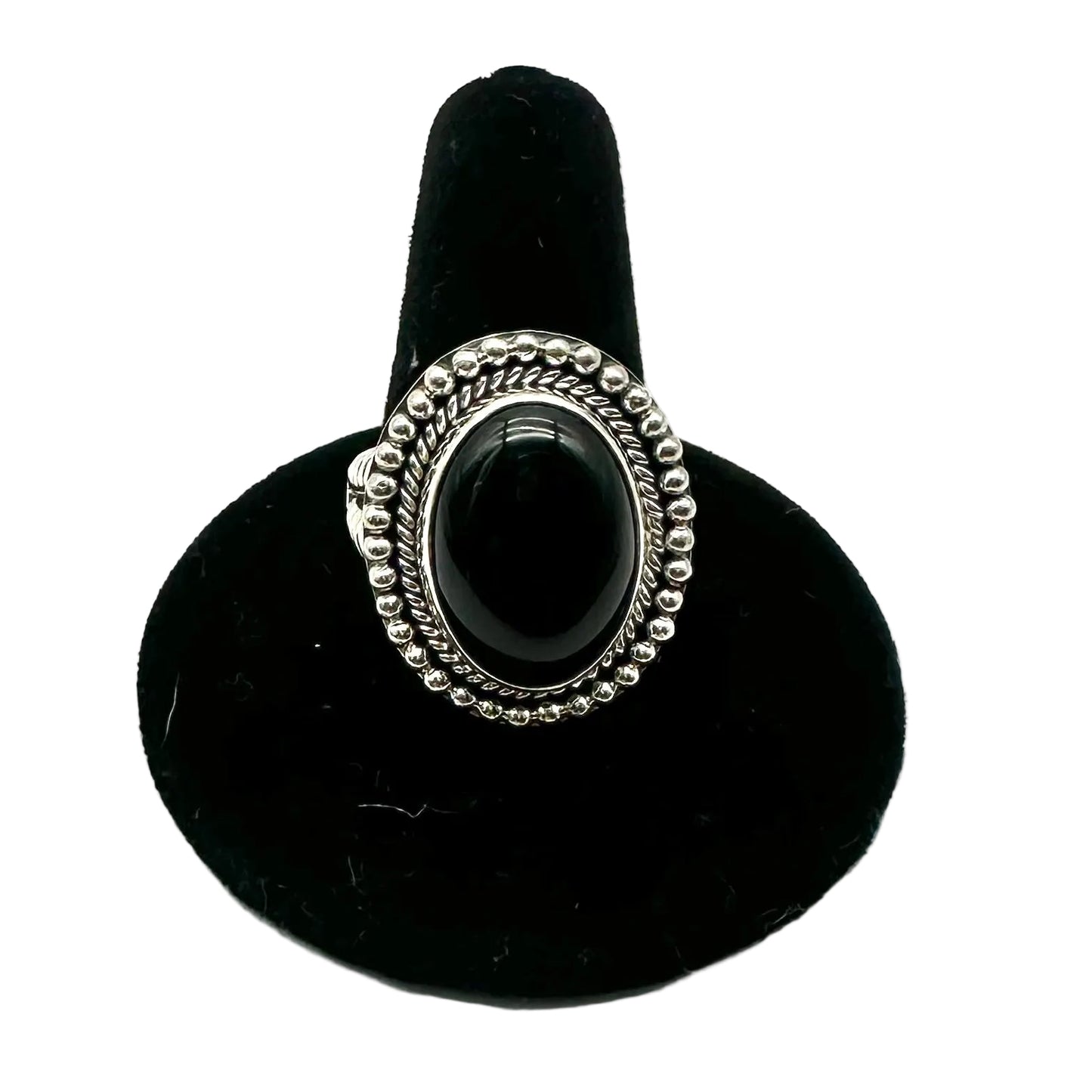 A silver-toned ring with an oval black cabochon stone, displayed on a black velvet ring stand against a white background.